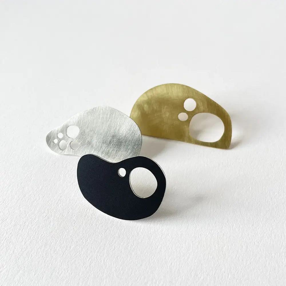 Set of three pins in mixed metals. Each an abstract sculptural shape with holes inside.