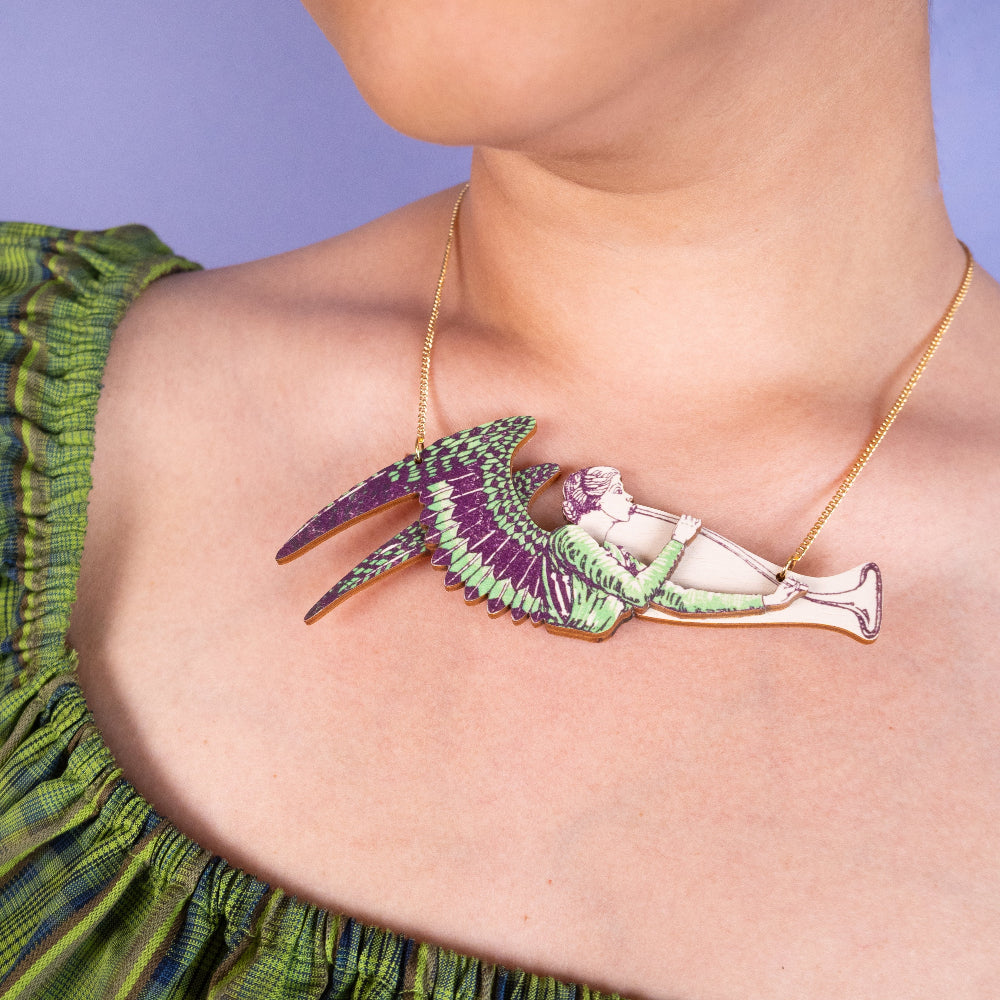 Person wearing a green dress with a gold necklace featuring a colorful pendant.