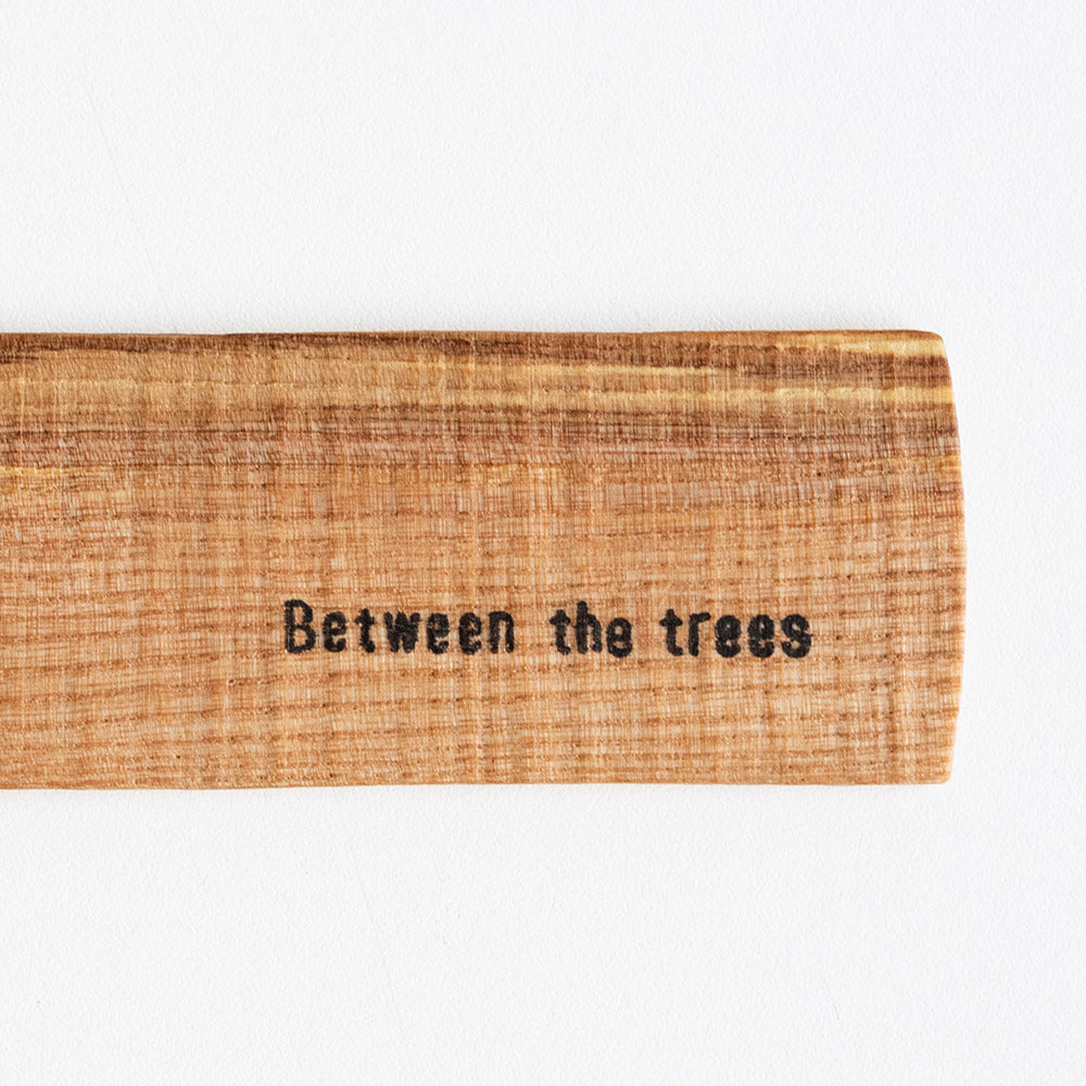 Wooden sign with 'Between the trees' text on a white background