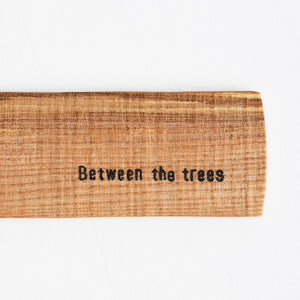 Wooden sign with 'Between the trees' text on a white background