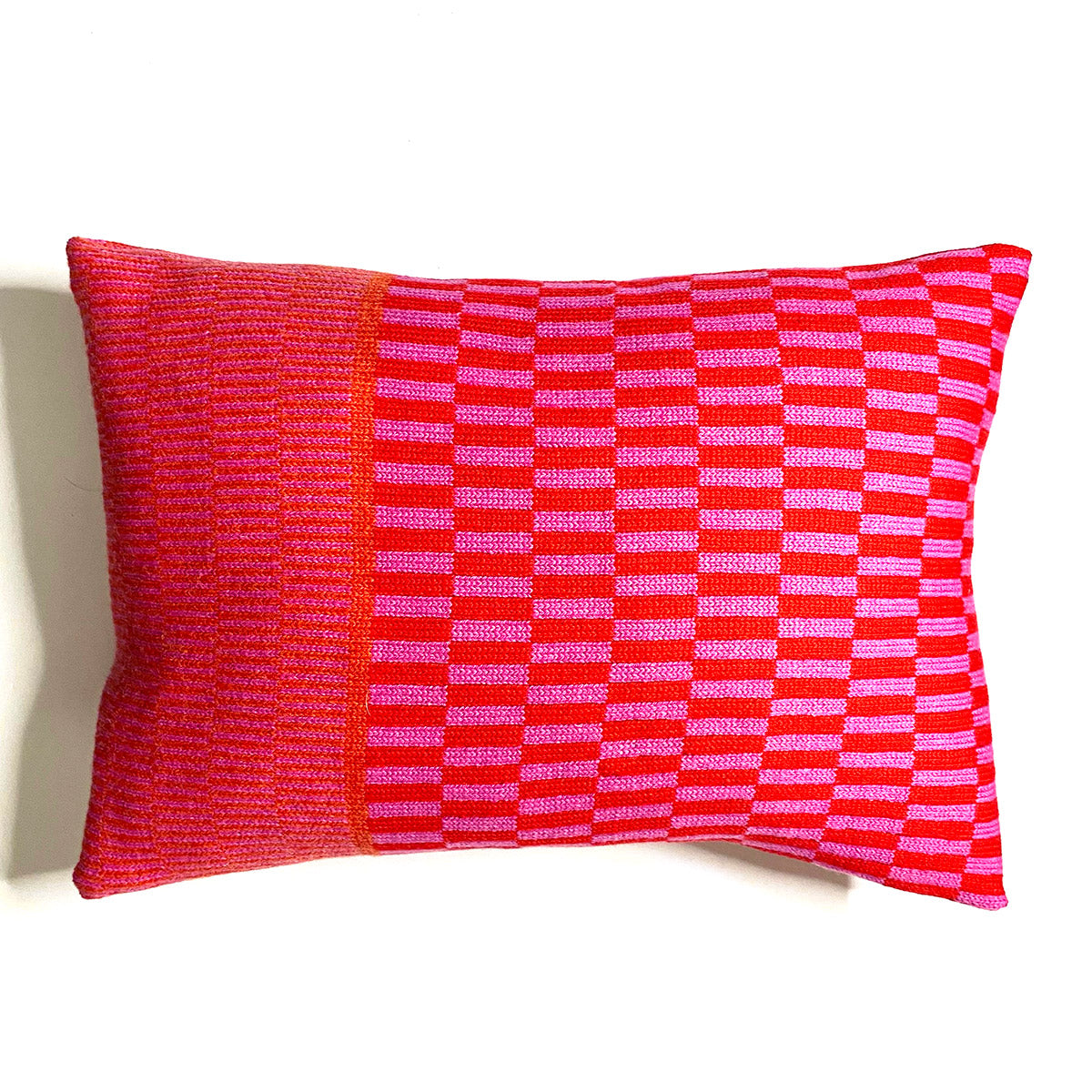 A rectangular pillow with a bold pink and red geometric pattern. The pattern is a combination of stripes and checks.