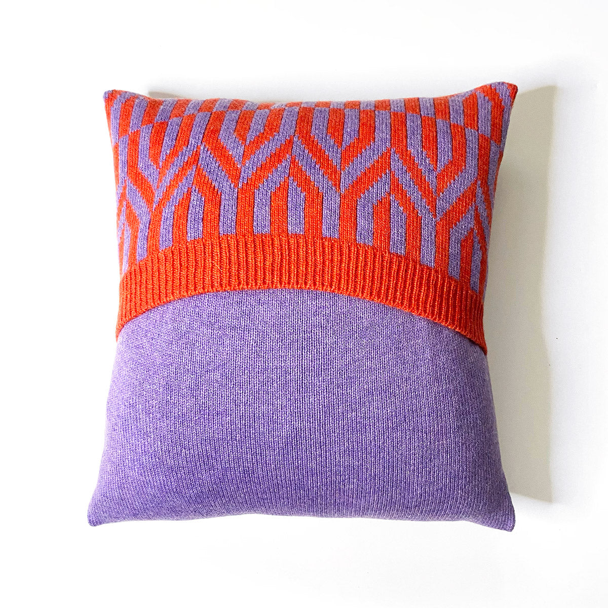 A square pillow with a bold orange and purple geometric pattern. The pattern is concentrated on the top half of the pillow, with a solid purple bottom half. The geometric shapes on the top half resemble arrows pointing in different directions.