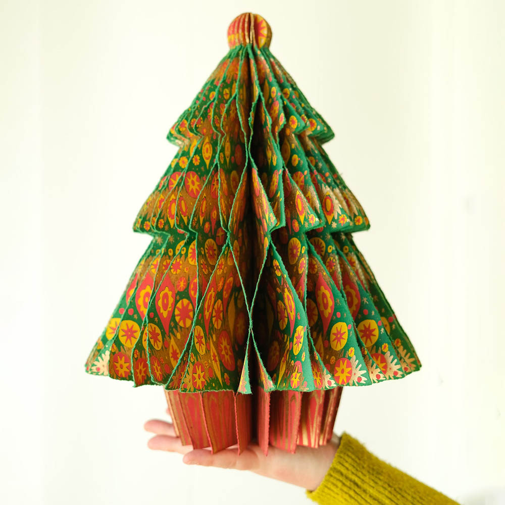 Hand holding a colourful paper Christmas tree against a white background