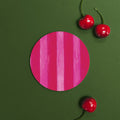 Red and pink striped coaster against a green background