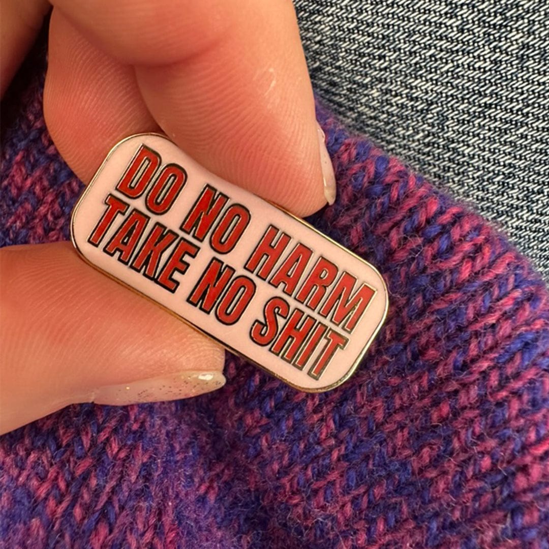 Person holding an enamel pink with red 'DO NO HARM TAKE NO SHIT' on a baby pink background.