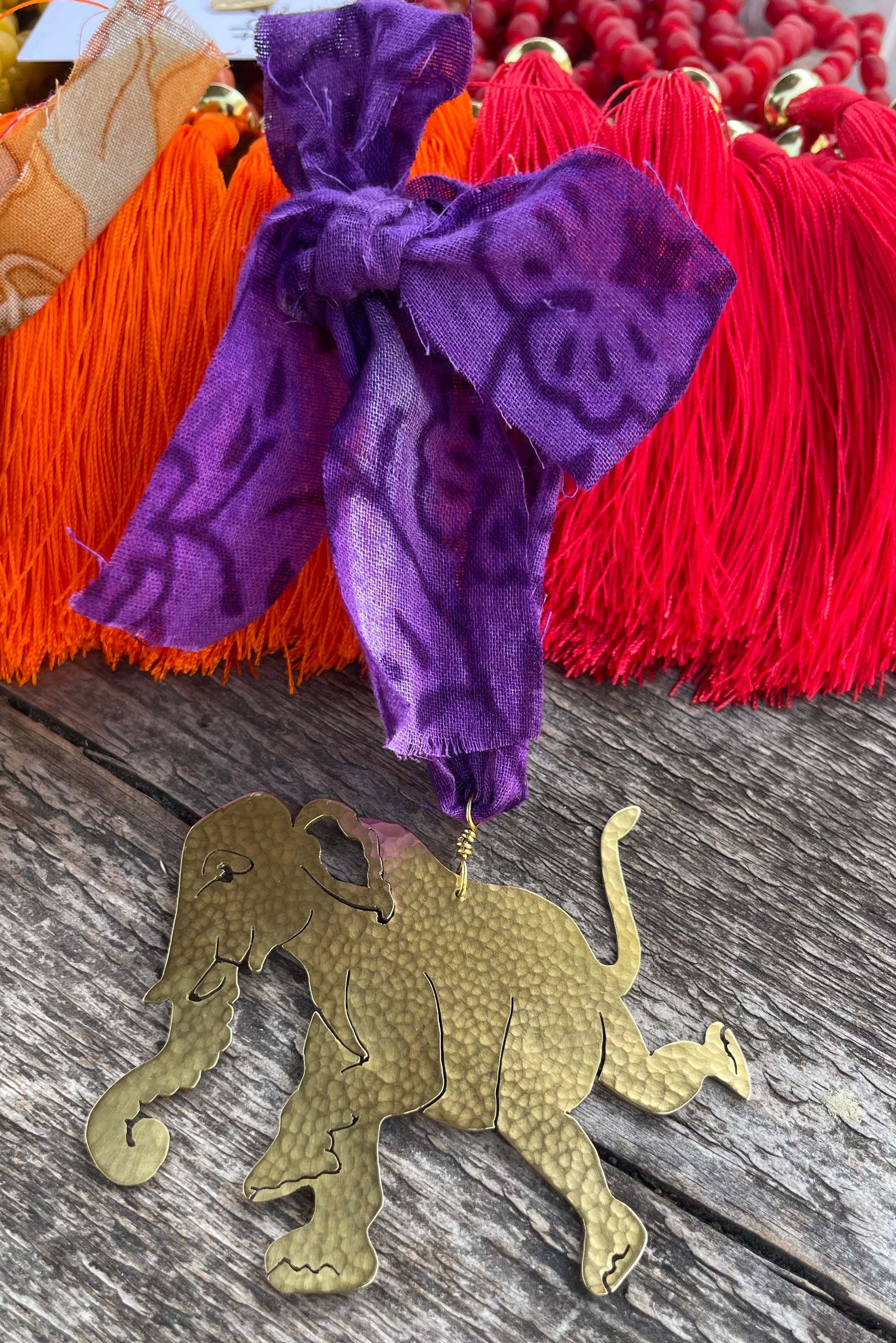 Lifestyle of brass elephant decoration with a purple fabric ribbon and lying on a woodne surface.