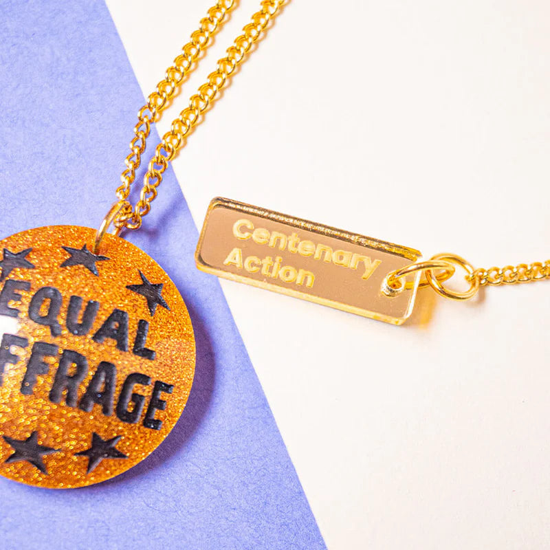 Gold necklace with 'Equal Suffrage' pendant on a purple and white background