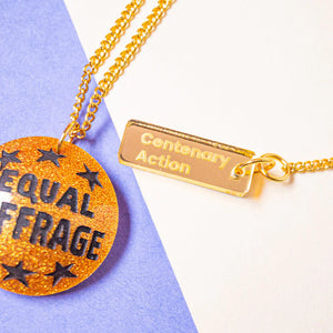 Gold necklace with 'Equal Suffrage' pendant on a purple and white background