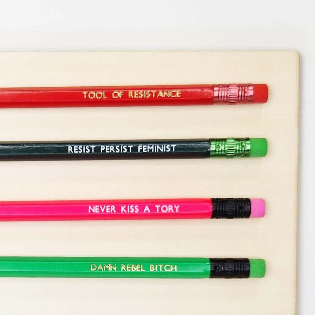 Four colourful pencils with feminist slogans are arranged diagonally on a light background.