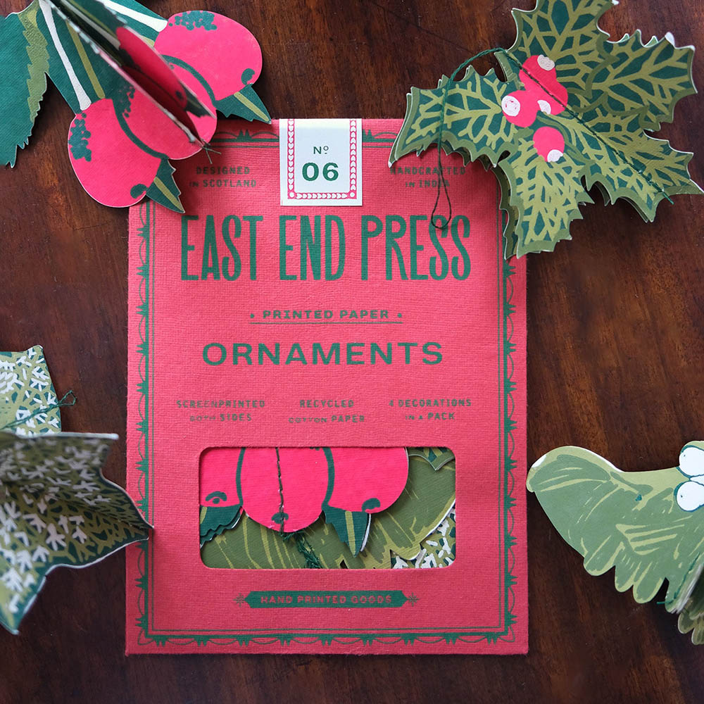 Packaging of East End Press printed paper ornaments on a wooden surface with decorative paper cutouts.