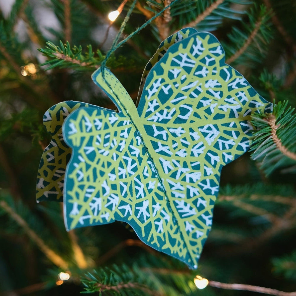 Decorative leaf ornament with green and white pattern hanging on a Christmas tree.