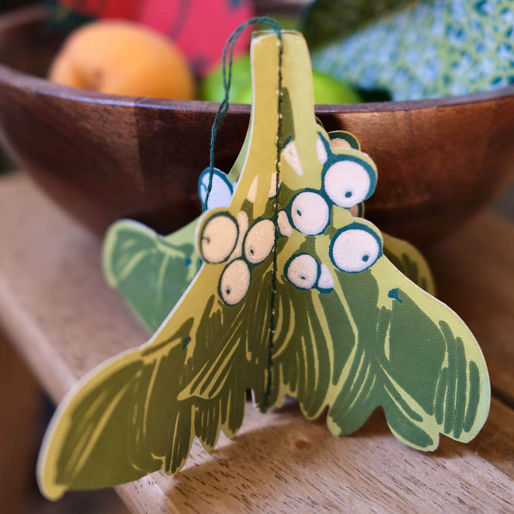 Two green paper moths with googly eyes on a wooden surface.