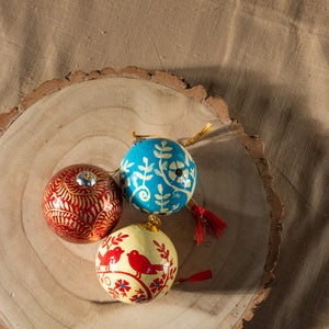 3 Baubles photographed from a birds-eye view sat on a circular tree trunk chopping board.