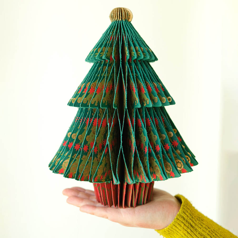 Hand holding a green and red patterned paper Christmas tree against a white background
