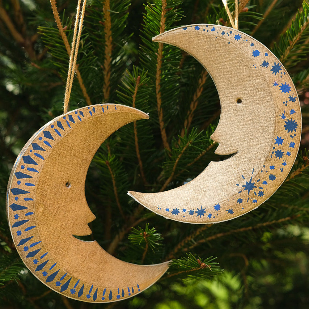 Gold moon-shaped ornaments with blue star patterns hanging on a Christmas tree.