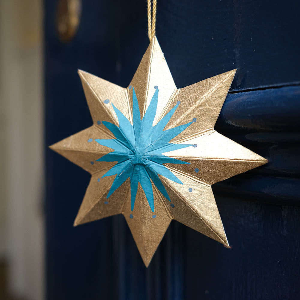 Decorative star ornament with gold body and blue center hanging against a dark background