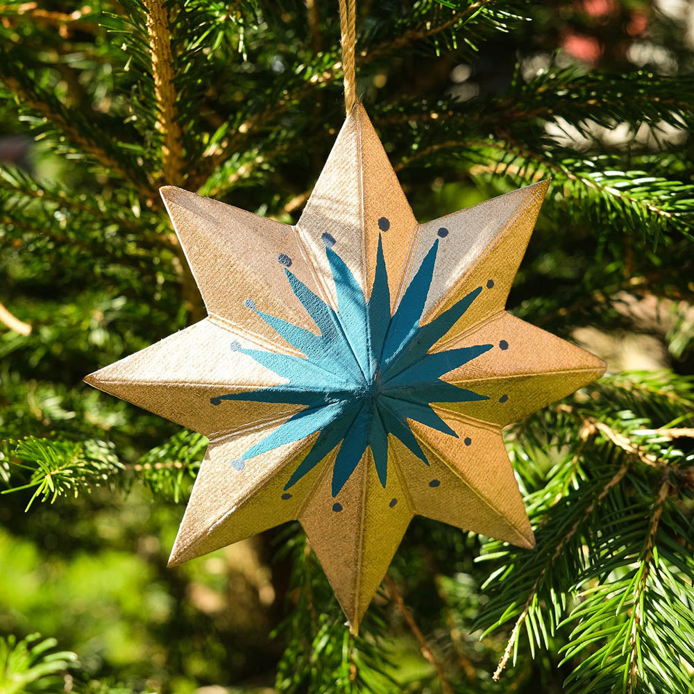 Star-shaped ornament with blue center and beige edges hanging on a tree.
