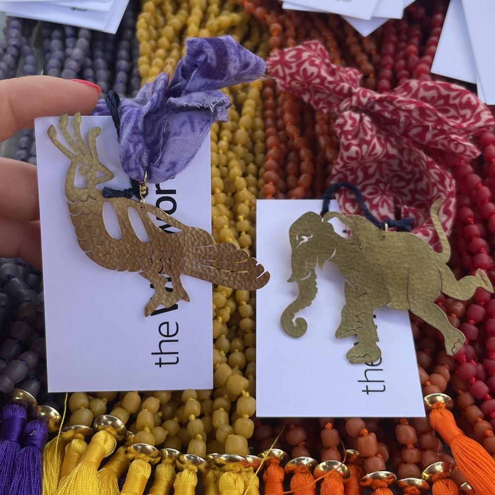 Two brass decorations in front of colourful beaded necklaces. To the left is a peacock and th eright is an elephant.