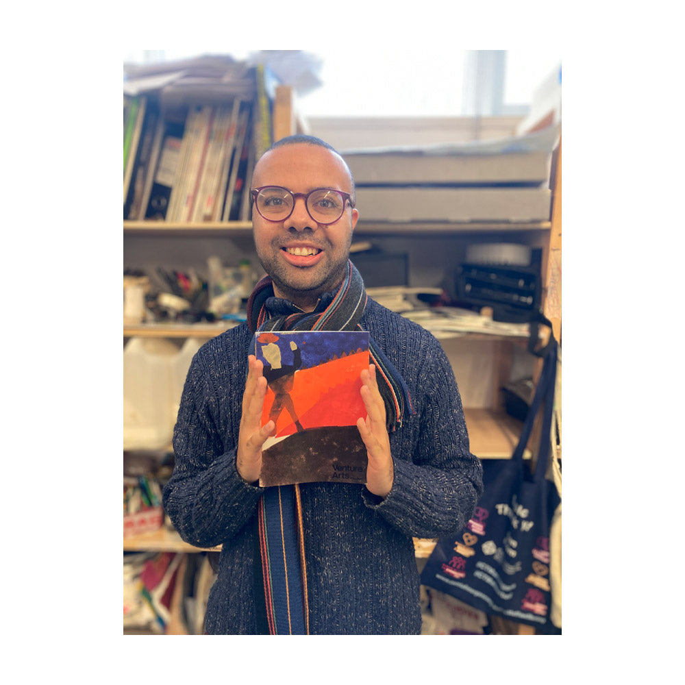 Josh Brown holding his zine and smiling at the camera.