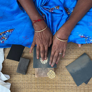 A person sanding an earring in the shape of a tropical leaf