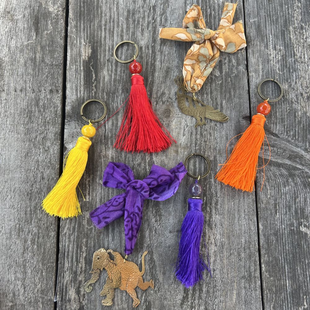 Colorful tassel keychains and two brass animal decorations on a wooden surface