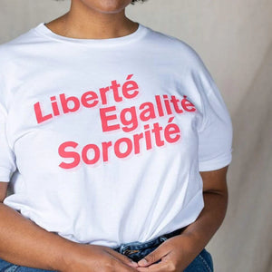 A person wearing a plain white t-shirt displays the French slogan "Liberté, Egalité, Sororité" in bold red letters.