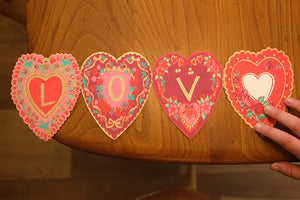 A concertina greetings card unfolded. Each panel is a letter spelling out the word LOVE.