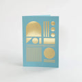 A light blue greeting card with gold foil geometric shapes, including circles, rectangles, and arches.
