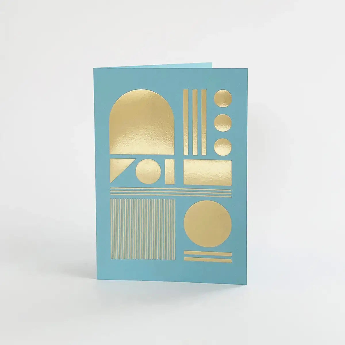 A light blue greeting card with gold foil geometric shapes, including circles, rectangles, and arches.