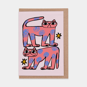 This is a white greetings card with a drawing of two pink cats with blue flower-like spots and yellow stars around them.