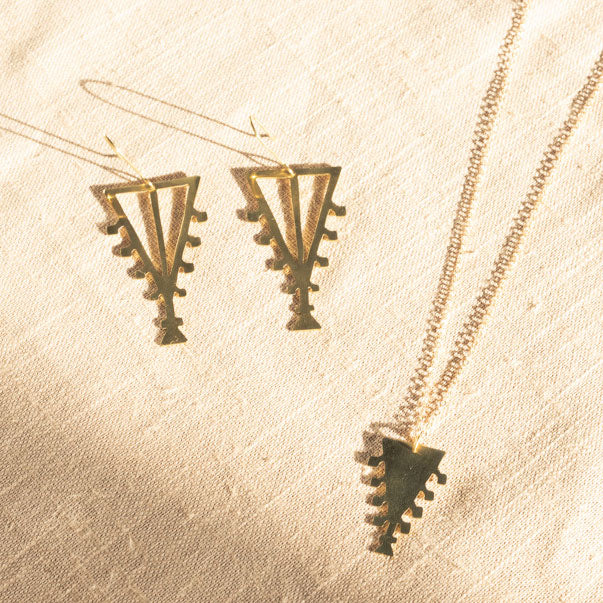 Lifestyle photograph of triangular earrings and pendant with chain, photographed on a linen tablecloth