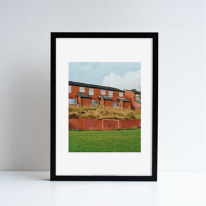 A framed reproduction of a photography work by Megan Dalton, featuring red bricked houses.