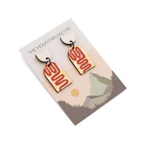 Dangly earrings photographed against Mountain and Me branded backing card and awhite background. The earrings are each in two pieces, the top a white semi-circle and the bottom an arch-shape with hand-painted red swirls.
