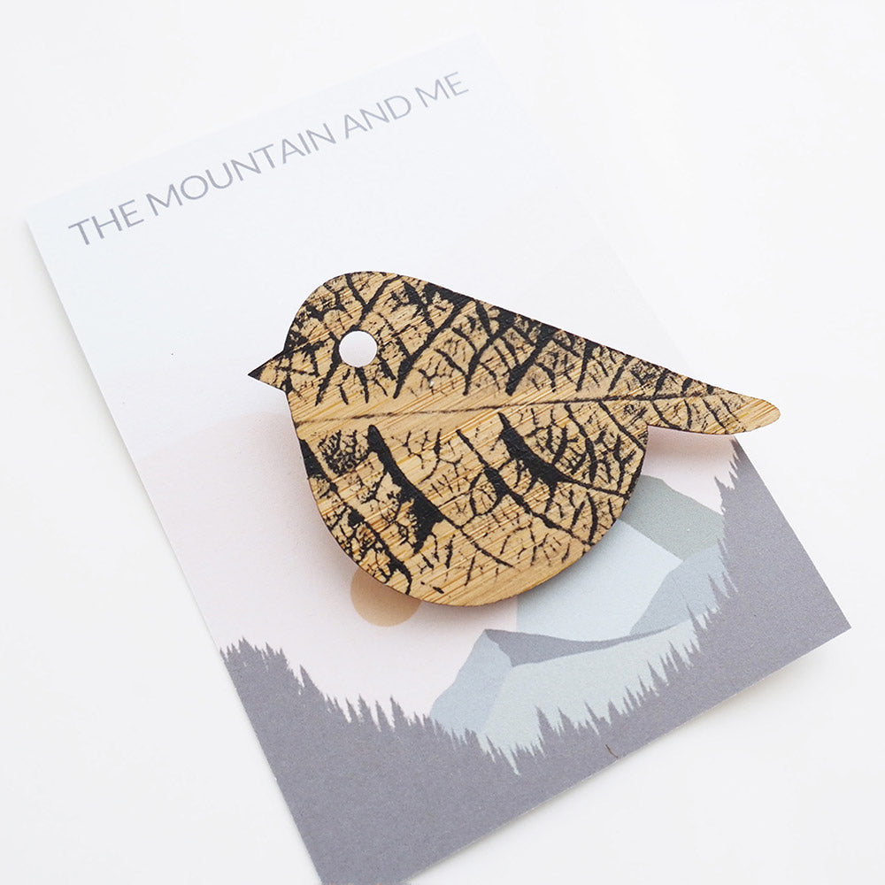 Wooden brooch in the shape of a bird against The Mountain and Me branded backing card