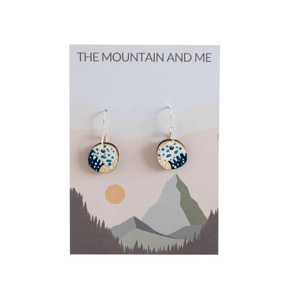 Circular wooden earrings with wave painted detail, on a branded backing card against a white backdrop