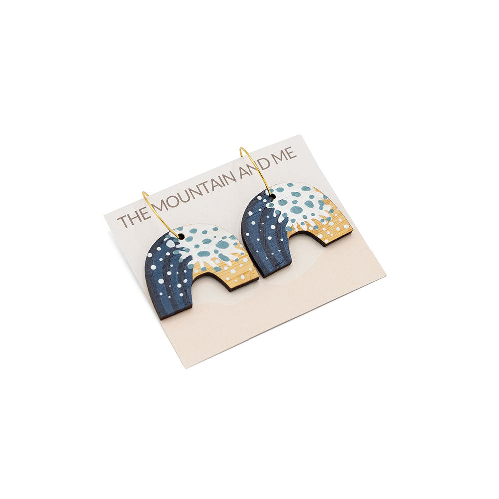 Arch-shaped wooden earrings wive wave painted detail, photographed against branded backing card on a white backdrop.