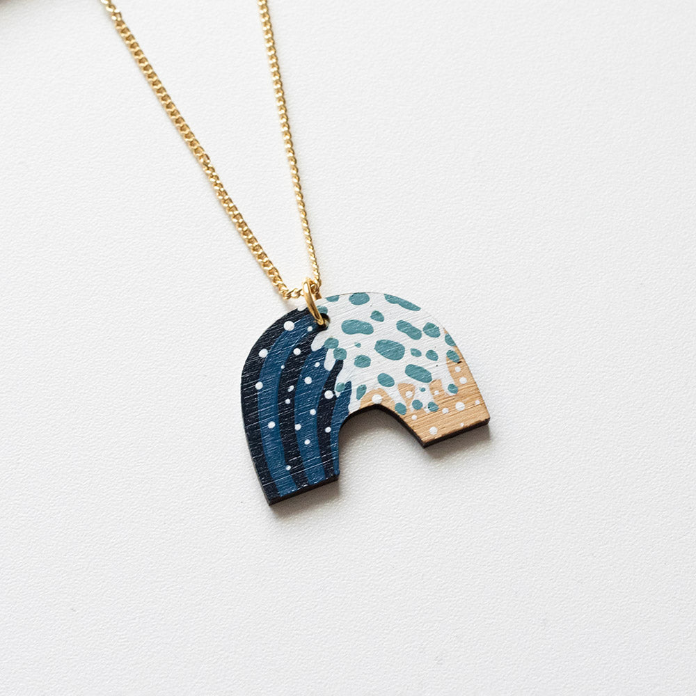 Wooden pendant in the shape of an archway, with wave painted detail and gold chain.