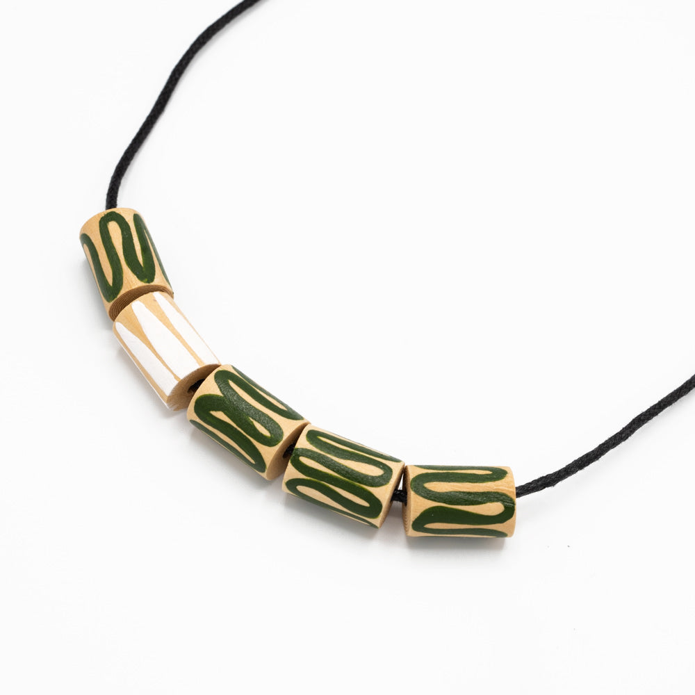 Close up photograph of  Necklace with thread chain against white background. Circular shapes threaded through the necklace made of wood, hand-painted with green and white swirls.