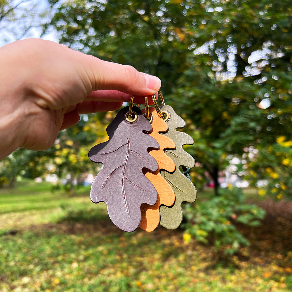 Person holding three leather leaf-shaped keyrings in front of a tree
