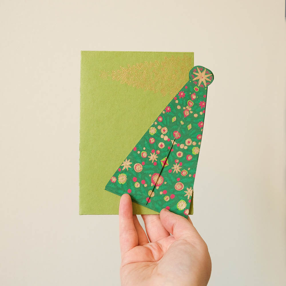 Hand holding a green card in the shape of a tree with floral design on a beige background