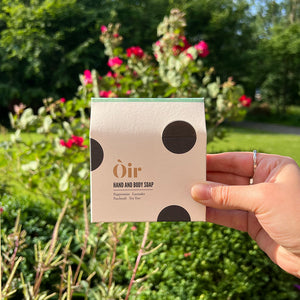 A person holding up a soap in its square package in front of some foliage