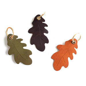 Three leaf-shaped earrings in green, brown, and orange on a white background