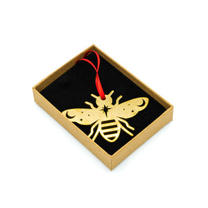 Brass bee decoration and red ribbon in a small brown box on a black cushion, White background.