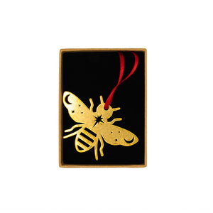 Brass bee decoration and red ribbon in a small brown box on a black cushion, White background.