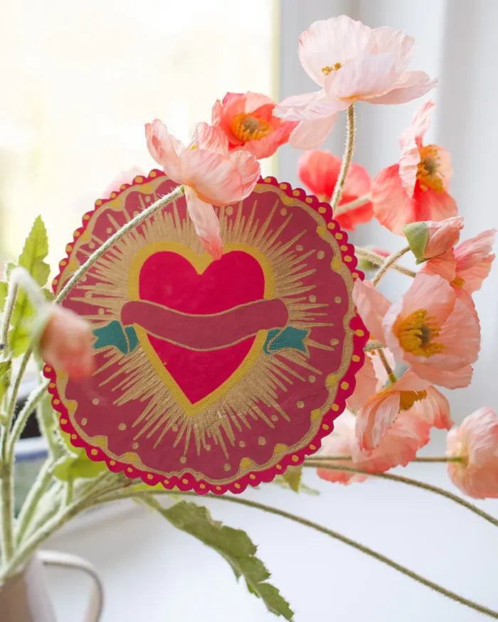 Circular greetings card with a love heart on it, placed amongst some pink flowers..