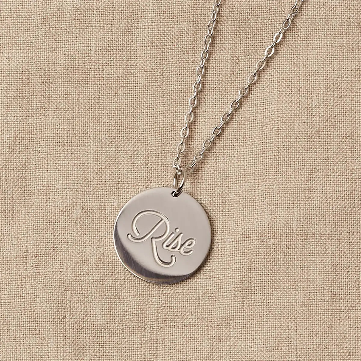 A stainless steel necklace with a circular pendant engraved with the word "Rise."