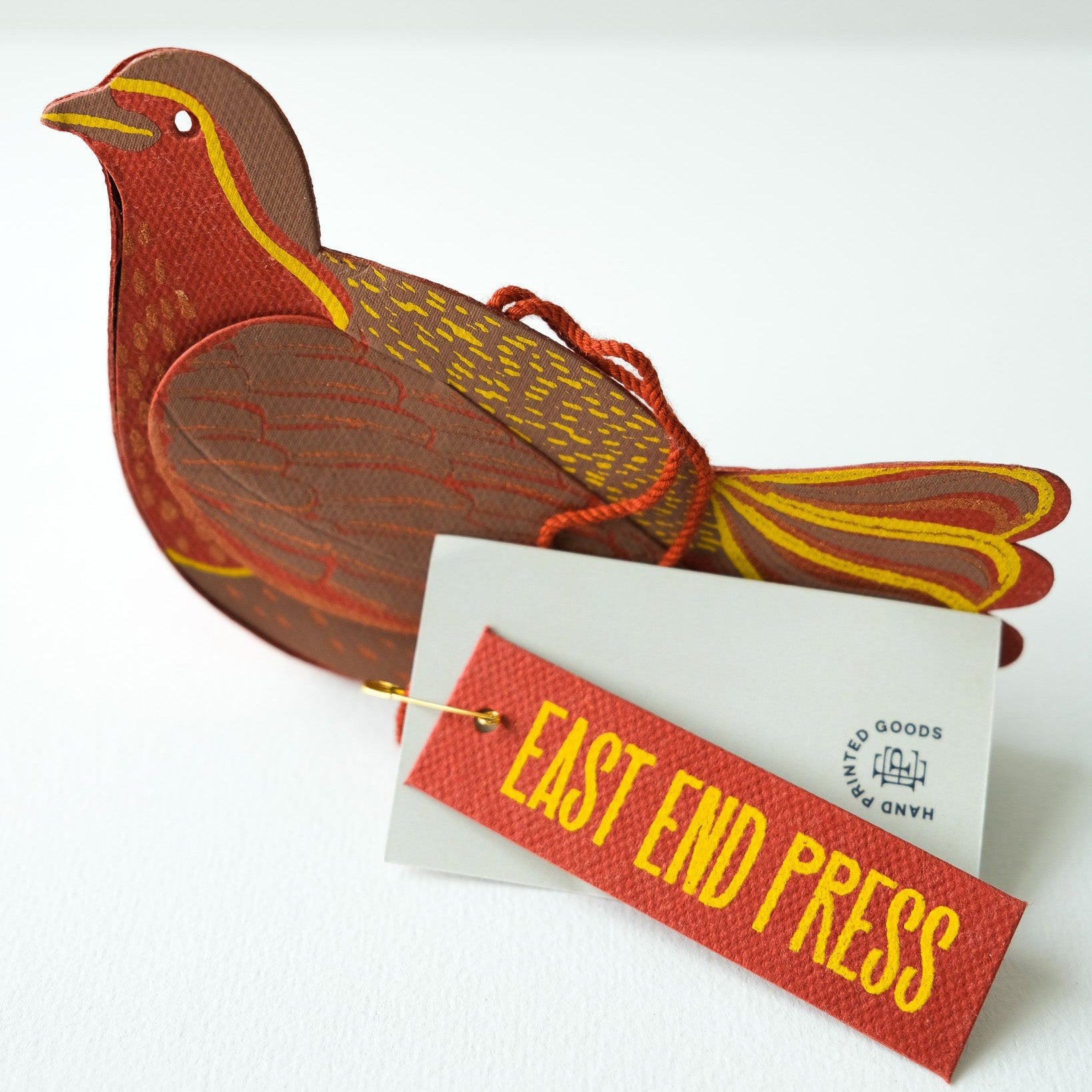 Decorative bird-shaped object with a tag labeled 'East End Press' on a white background