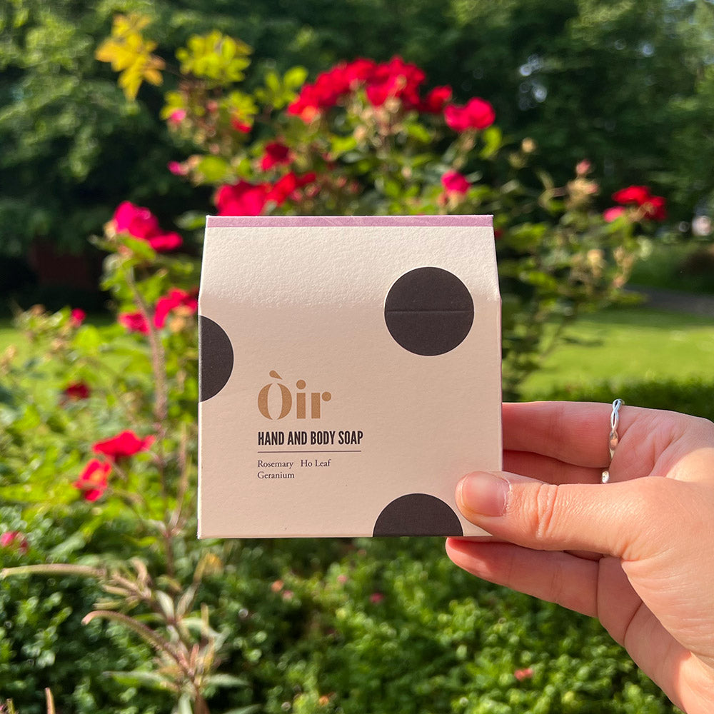 A person holding up a soap in its square package in front of some foliage