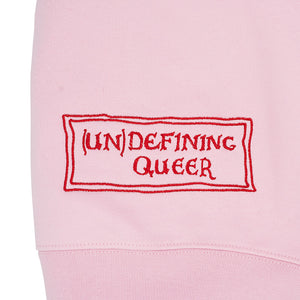 Close up of a pink jumper with the Un Defining Queer logo embroidered in red thread.