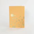 A peach-coloured greeting card with gold foil geometric shapes, including circles, rectangles, and lines, scattered across the card.